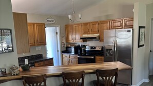 A modern kitchen with wooden cabinets, a stainless steel refrigerator, a built-in oven, and a bar area with three stools. - Surfside Hideaway! Dog friendly 3 bed, 2 bath home. Only 1 mile to beach! (Myrtle Beach)
