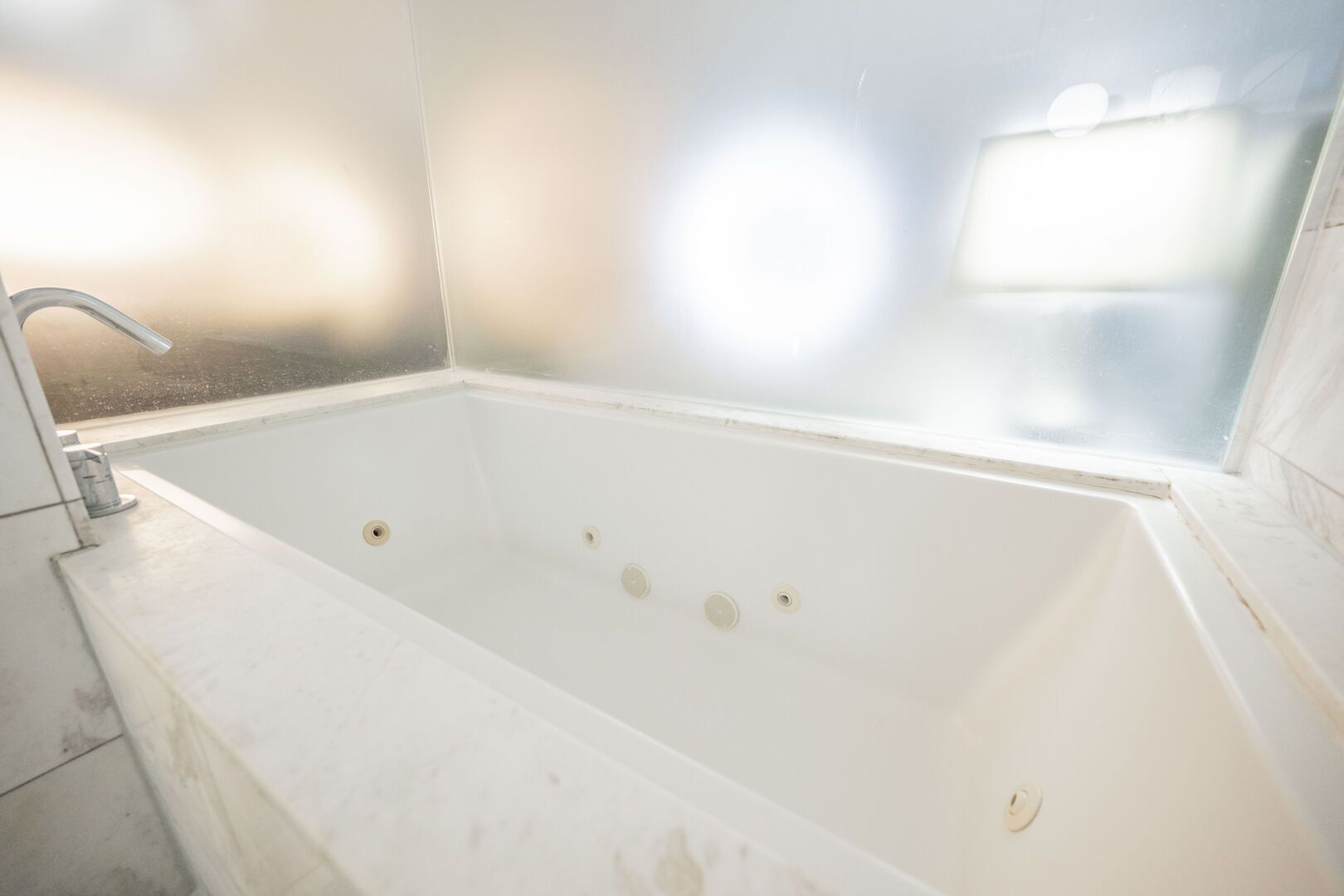 Una vasca da bagno bianca con un singolo rubinetto, una finestra sopra e un muro rivestito di piastrelle.