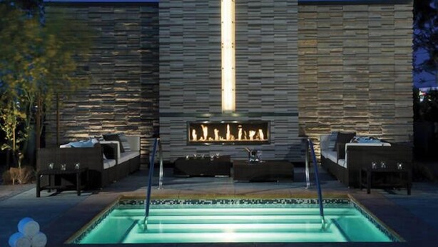 An outdoor pool area with a stone wall, seating, and a fire feature. - SVS: Strip View Studio | Open Balcony | Pool Access | Palms Place (Las Vegas)