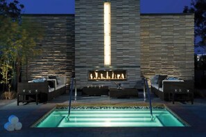 Un espace extérieur avec une piscine, un mur en pierre, des sièges et un foyer.