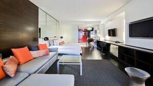 Ein modernes Hotelzimmer mit einer Couch, einem kleinen Couchtisch, einem Fernseher und einer Küchenzeile.