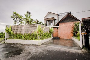 A modern house with a wooden door, a concrete garden bed with plants, and a paved driveway.