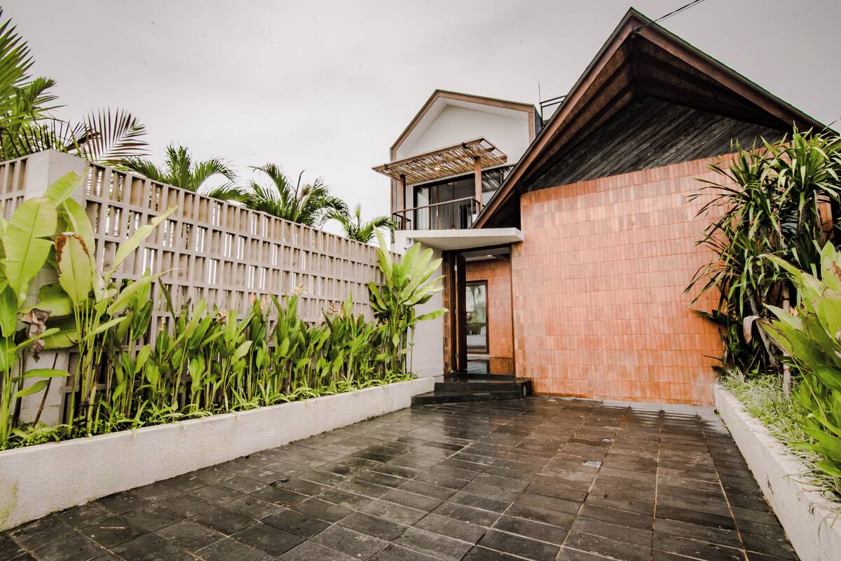 A modern house with a tiled patio, a wooden fence, and lush greenery.