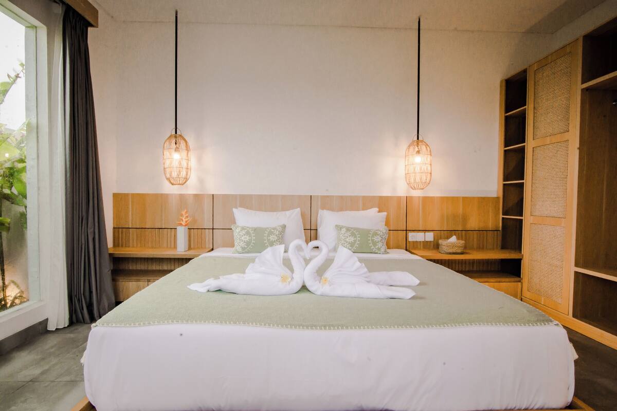 A hotel room with a large bed, two bedside tables, a wooden wardrobe, and a window with curtains.