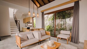 Un salón amplio con un sofá, una mesa de centro y una silla. Se ve una escalera que conduce a un nivel superior.