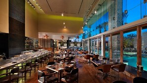Ein geräumiges Restaurant mit einer langen Theke, mehreren Tischen und Stühlen. Große Fenster bieten Blick auf einen Swimmingpool.