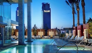 A swimming pool area with lounge chairs, palm trees, and a tall building labeled 'PALMS' in the background. - SVS: High Floor Strip View Studio | Open Balcony | Palms Place (Las Vegas)