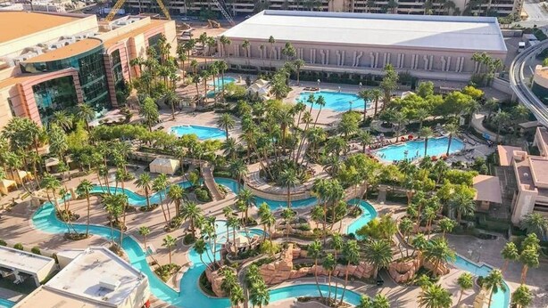 Luftaufnahme eines Resorts mit mehreren miteinander verbundenen Schwimmbecken, umgeben von Palmen und angelegten Grünflächen.