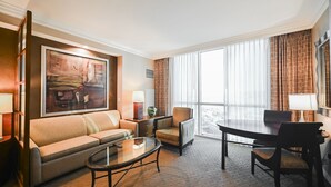 A hotel room with a sofa, a small table, a dining table with chairs, a large window with curtains, and a painting on the wall. - SVS: Strip View Studio | Pool & Gym Included | No Resort Fee | MGM (Las Vegas)