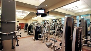 A gym with various exercise machines, a television mounted on the ceiling, and a mirror on the wall. - SVS: Strip View Studio | Pool & Gym Included | No Resort Fee | MGM (Las Vegas)