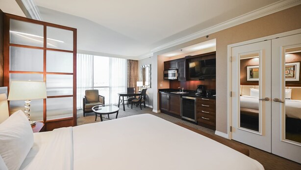 A hotel room with a large bed, a dining table with chairs, a kitchenette, and a separate bedroom area. - SVS: Strip View Studio | Pool & Gym Included | No Resort Fee | MGM (Las Vegas)