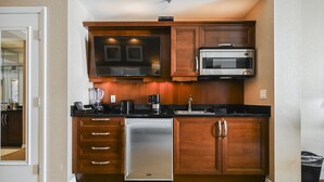 A compact kitchen with wooden cabinets, a stainless steel refrigerator, a microwave, and a coffee maker. - SVS: Strip View Studio | Private Balcony | Pool & Gym | Signature at MGM (Las Vegas)