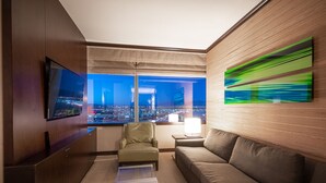 Quarto de hotel moderno com uma grande janela com vista para a cidade, uma TV de tela plana, uma poltrona de couro, um sofá e uma mesa de centro.