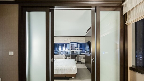Ein modernes Hotelzimmer mit Blick auf die Stadt, ausgestattet mit einem Bett, einem Schreibtisch und einem großen Fenster.