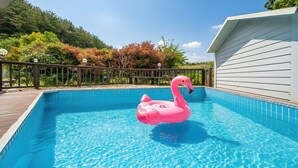Ein Swimmingpool mit einem Schwimmflamingo, umgeben von einer Holzterrasse und einem weißen Gebäude.