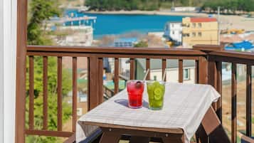 A balcony with a table set for two, overlooking a coastal area with buildings and a blue body of water.