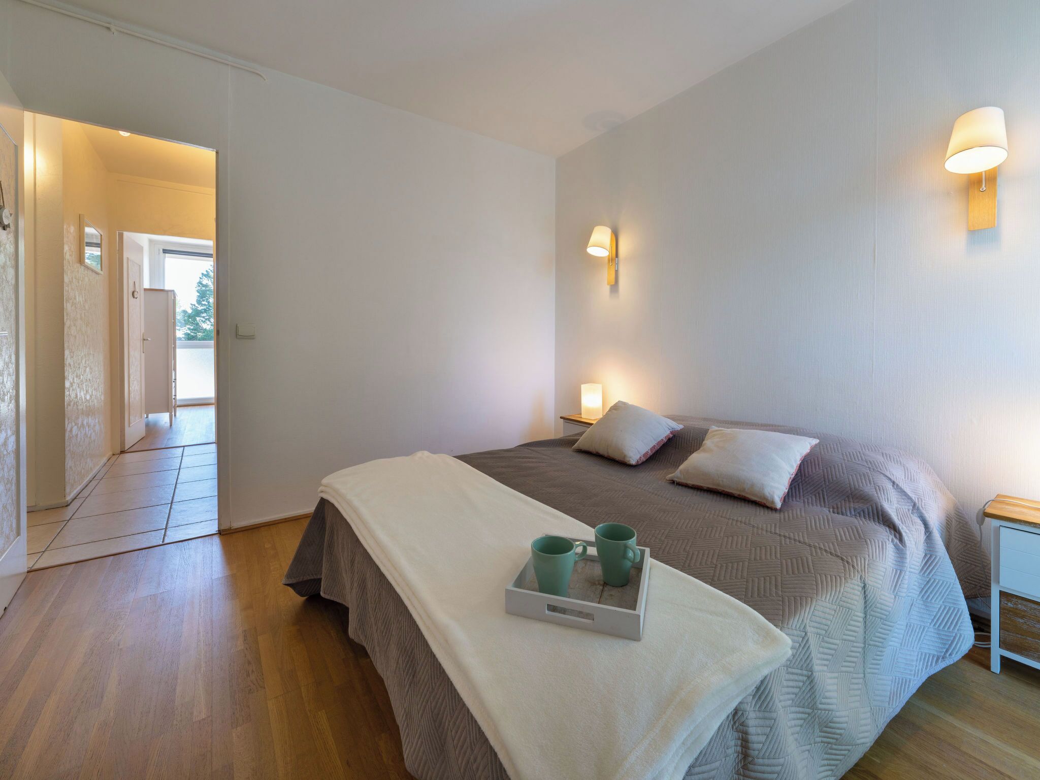 Ein Schlafzimmer mit einem Bett, Nachttischlampen, einem Tablett mit Tassen und Holzboden.