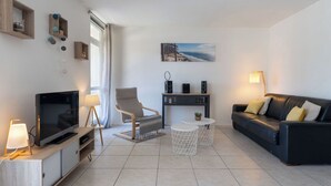 A modern living room with a flat-screen TV, a sofa, a chair, a coffee table, and a small side table with a lamp. - Arcachon Marines by Interhome (Arcachon)