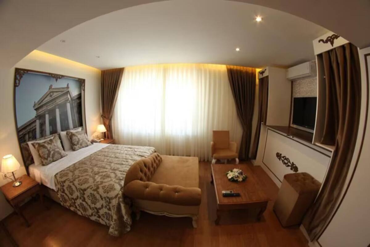 A hotel room with a bed, a sofa, a desk, a chair, and a TV.