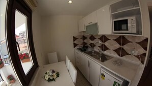 Una cocina compacta con armarios blancos, un microondas y un lavabo. Hay una mesa de comedor con un florero.