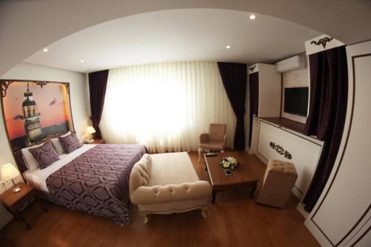 A hotel room with a large bed, a sitting area with a table and chairs, a TV, and a painting of a mosque.