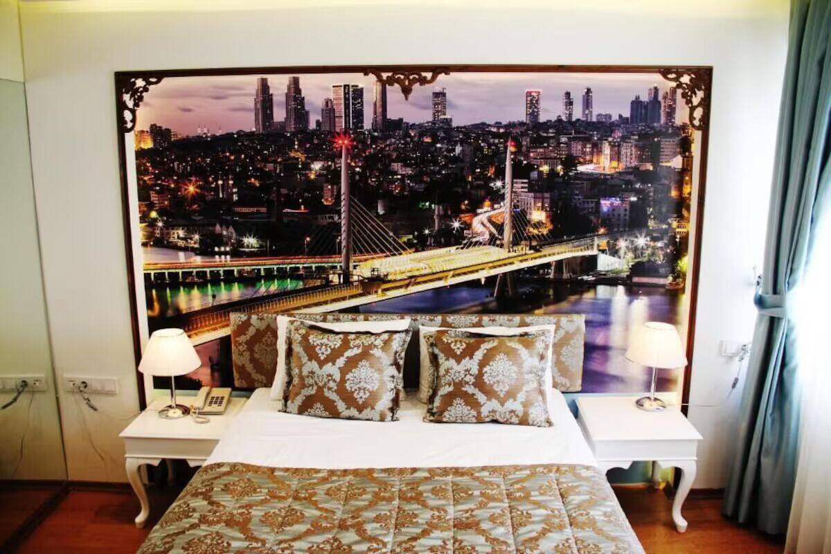 A hotel room with a cityscape view, a bed with patterned bedding, two bedside tables with lamps, and a curtain on the right.
