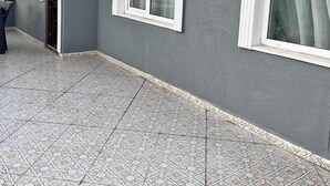 Un edificio con fachada gris, ventanas de marco blanco y suelo de baldosas estampadas.