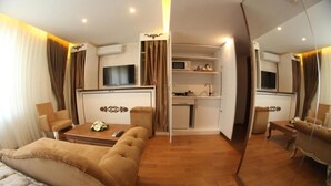 Habitación de hotel compacta con sofá, una mesita, televisión, kitchenette y espejo.