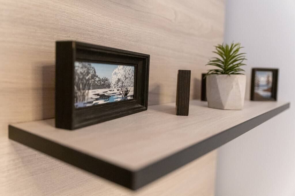 Una estantería con un cuadro enmarco, una planta en maceta y un pequeño florero.