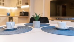 A modern dining area with a white table, two white cups, a small potted plant, and a TV in the background.