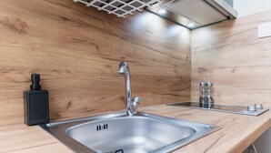 A modern kitchen with a stainless steel sink, wooden backsplash, and a built-in range hood. - City Center Studio Apartments 1 (Plovdiv)
