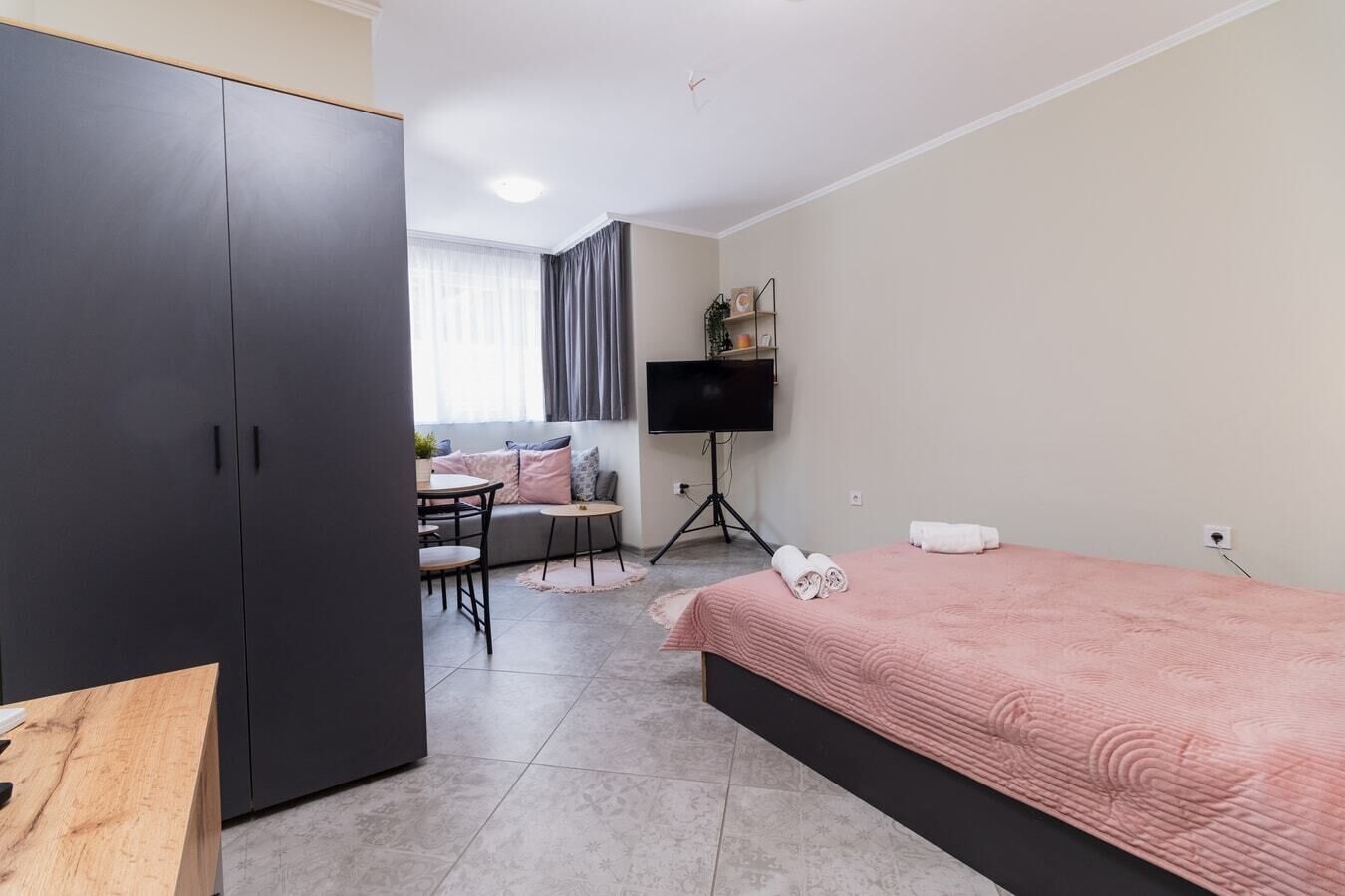 A compact hotel room with a bed, a desk, a wardrobe, a TV, and a small seating area.