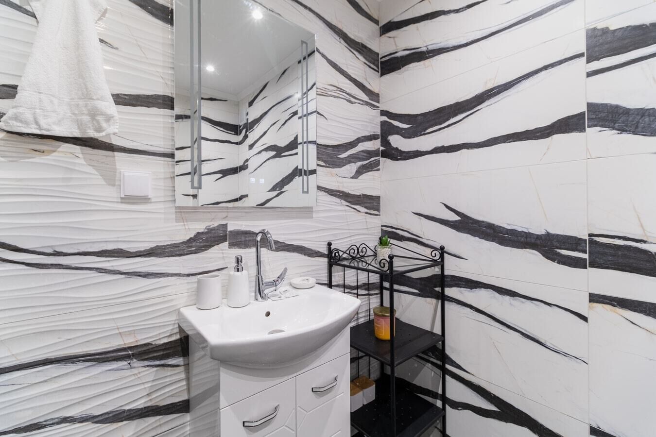 A modern bathroom with a marble vanity, a sink, a mirror, and a shelf with toiletries.