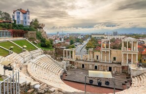 Experience the ancient charm of this historic amphitheater, set amidst a modern cityscape with a classical design featuring columns and tiered seating.