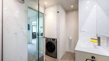 Un baño moderno con cabina de ducha de vidrio, lavadora integrada y lavamanos blanco con un toallero.