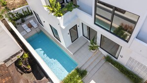 Una casa moderna de dos pisos con piscina, ventanas amplias y mobiliario exterior.