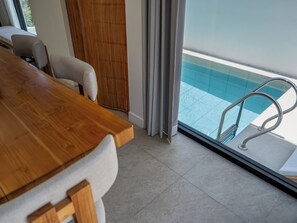 Una habitación moderna con una mesa de comedor de madera, un sofá y vistas a una piscina a través de grandes ventanales.