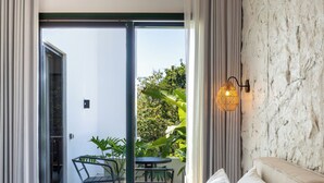 Un dormitorio moderno con una cama grande, vistas al exterior a través de una puerta corredera, una pequeña mesa con sillas y una lámpara de pared.