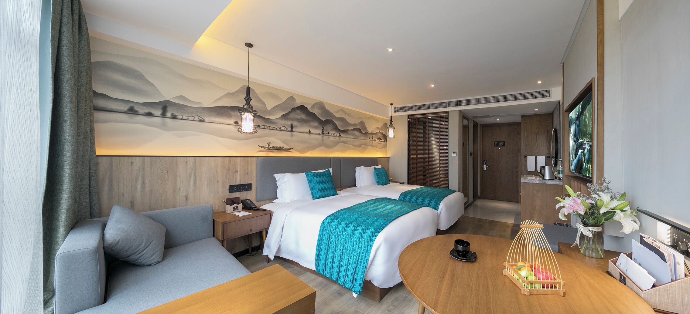 A hotel room with a large bed, a sofa, a dining table, and a wall mural.