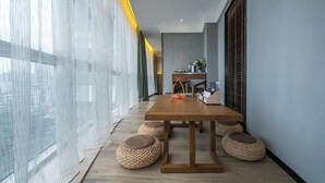 A modern dining area with a wooden table, woven stools, and a view of the city through sheer curtains. - Mehood Lestie International Hotel Chongqing Yuzhong Lianglukou Metro Branch (Chongqing)