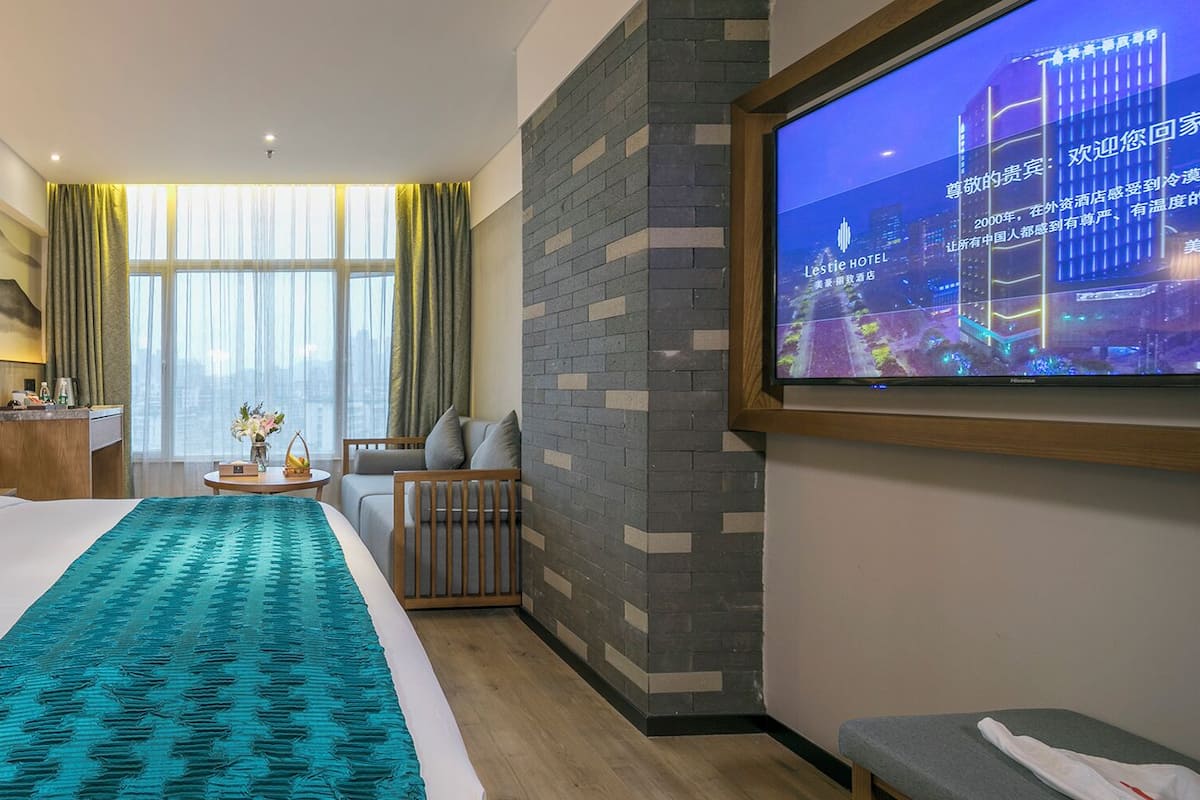 A hotel room with a large bed, a television, a desk, and a view of the cityscape.