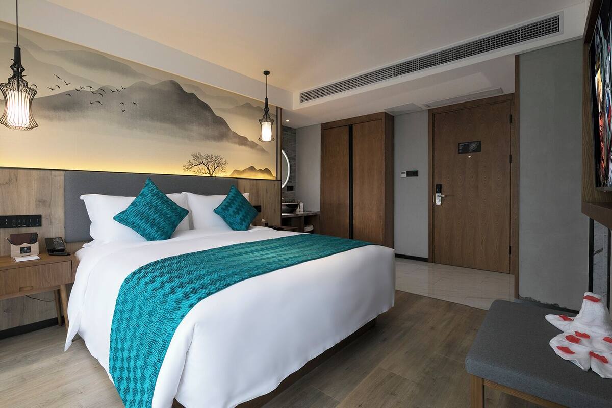 A hotel room with a large bed, a nightstand, a desk, a wardrobe, and a wall with a mural.