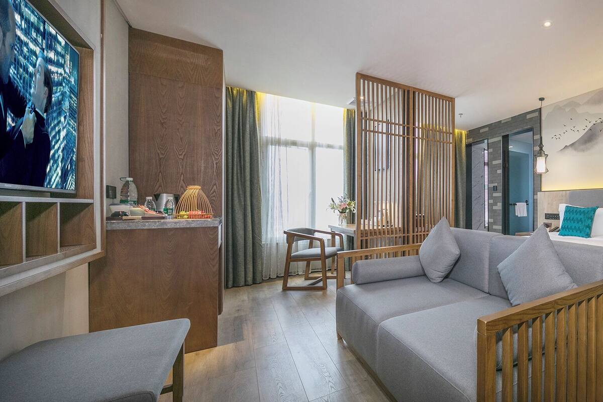 A modern hotel room with a sofa, a bed with teal pillows, a wooden partition, and a wall mural.