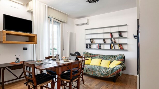 A modern living room with a wooden dining table, chairs, a sofa, a flat-screen TV, and a bookshelf. - GuestHost - Rimini Oasis of Peace & Relaxation! (Rimini)