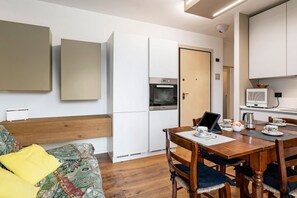 Une cuisine moderne avec des armoires blanches, un four encastré et un four à micro-ondes. On y trouve une table à manger avec des chaises et un ordinateur portable.
