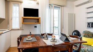 A dining area with a wooden table, chairs, a television mounted on the wall, and a window with curtains. - GuestHost - Rimini Oasis of Peace & Relaxation! (Rimini)