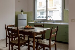 A kitchen with a dining table, chairs, a refrigerator, a window with a view of buildings, and a sink.