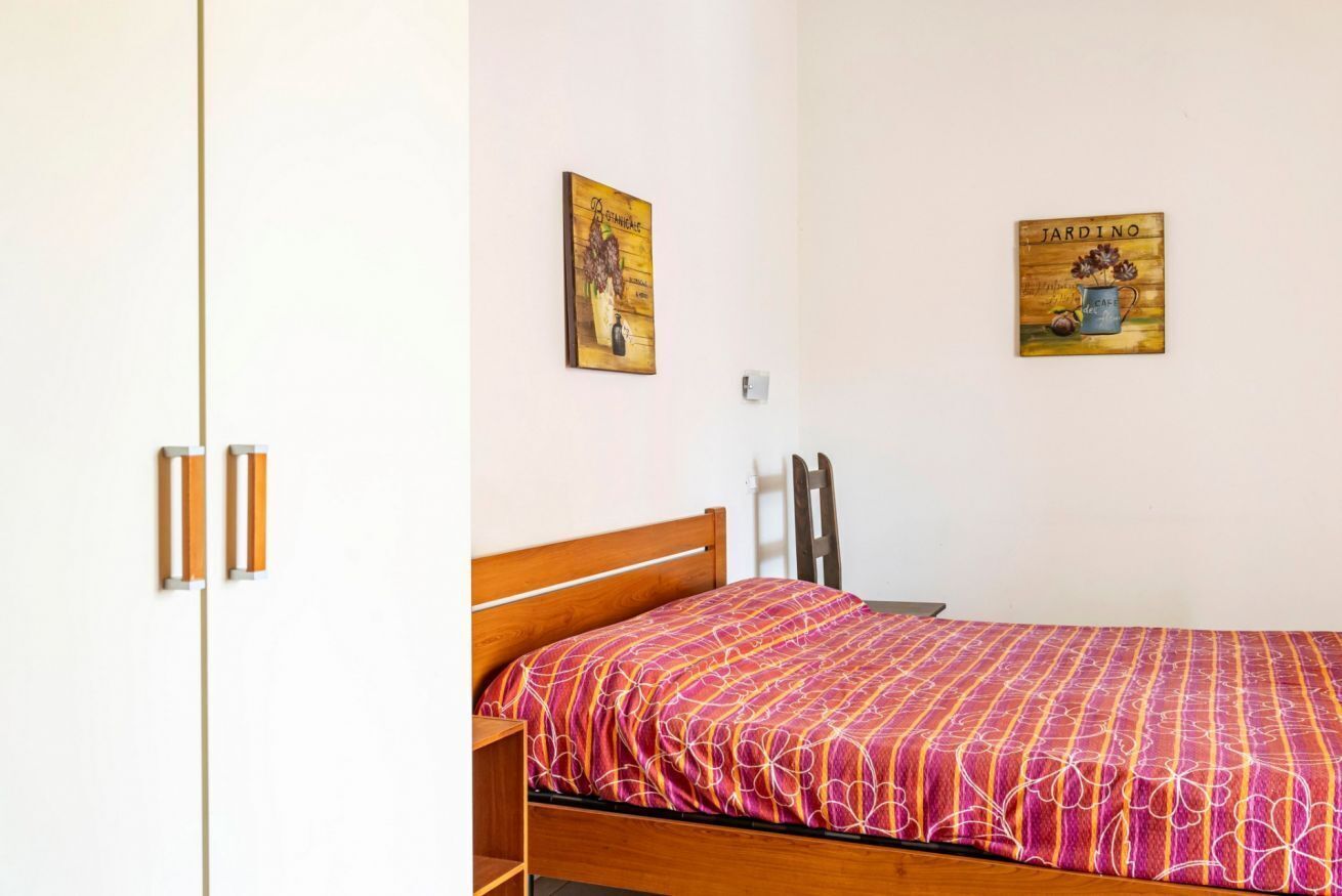 A single bed with a patterned bedspread, a wooden headboard, and two wall-mounted paintings.