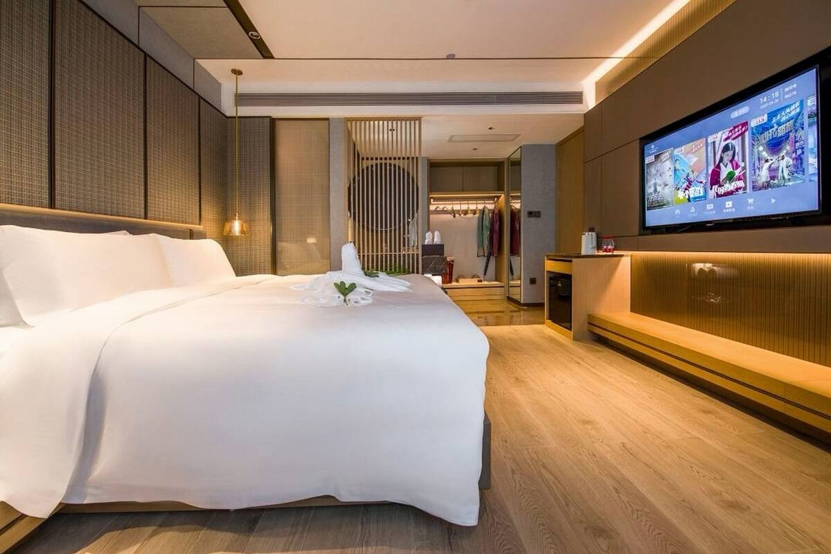 Une chambre d’hôtel moderne avec un grand lit, un téléviseur fixé au mur et un plancher en bois.