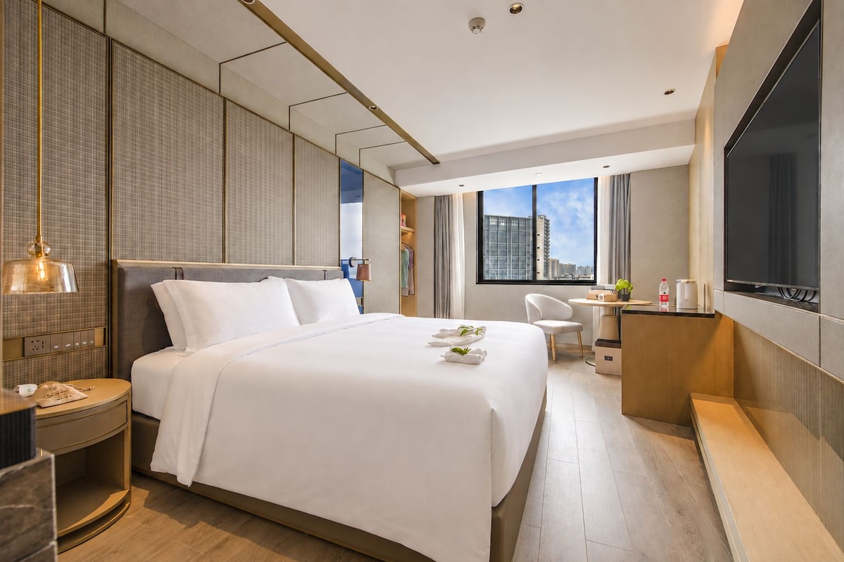 Et moderne hotelværelse med en stor seng, et skrivebord, en stol og et fjernsyn.